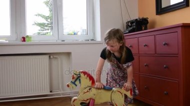 Sevimli küçük kız üzerinde sallanan at sallanır. Smalll kız çiçekli elbise giyer. Çocukluk kavramı