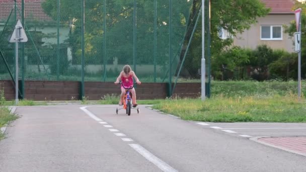 Chica monta la bicicleta en el tráfico del parque infantil. Niña en bicicleta en el verano — Vídeos de Stock