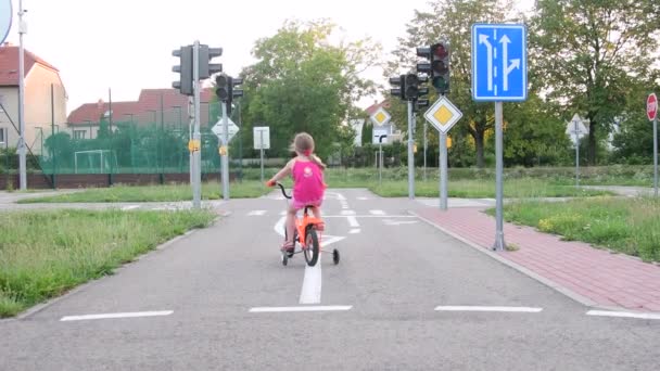 मुलगी खेळाच्या मैदानावर वाहतुकीच्या वेळी बाईक चालवते. उन्हाळ्यात बाईक वर लहान मुलगी — स्टॉक व्हिडिओ