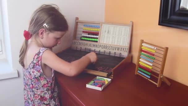Солодка дівчинка грає з abacus і пише на дошці з крейди. Дошкільного концепції, концепція дитинства. Іграшка abacus з чеської алфавіту. Кінематографічна відблиску — стокове відео