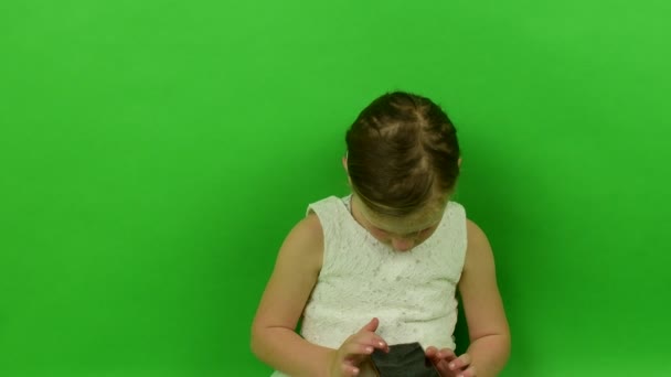 Linda niña pequeña utiliza el teléfono móvil en el fondo de croma key. Niña vestida con un vestido romántico. Vestido de novia blanco. Fondo clave de croma . — Vídeo de stock