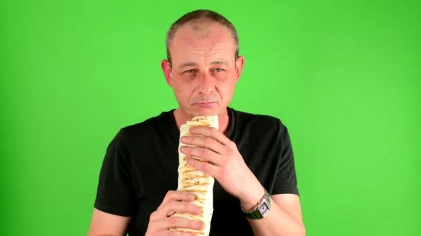 Homem maduro de meia idade. Retrato de um homem maduro come o fast food kebab também chamado giroscópios na frente da tela verde . — Vídeo de Stock