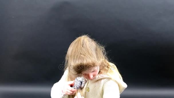 Menina bonito penteia o cabelo. Menina pequena está vestida com roupas de inverno. Menina bonito no fundo preto . — Vídeo de Stock