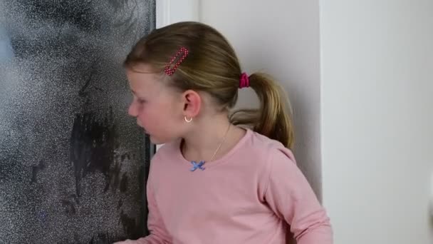 La fille dessine un doigt sur une vitre. Petite fille mignonne essuie fenêtre gelée en hiver . — Video