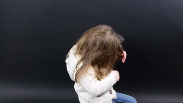 Menina bonito penteia o cabelo. Menina pequena está vestida com roupas de inverno. Menina bonito no fundo preto . — Vídeo de Stock