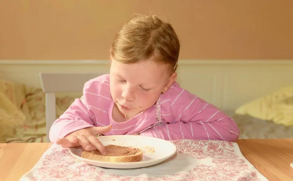 La chica feliz tiene un aperitivo en la cocina. Una linda niña pequeña sonríe. Una niña pequeña con manchas de crema de chocolate en la cara. Concepto de infancia y diversión . —  Fotos de Stock