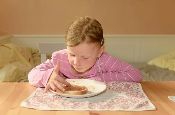 La chica feliz tiene un aperitivo en la cocina. Una linda niña pequeña sonríe. Una niña pequeña con manchas de crema de chocolate en la cara. Concepto de infancia y diversión . —  Fotos de Stock