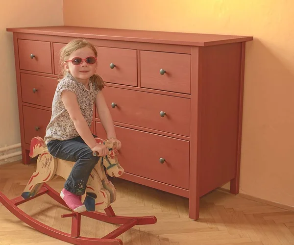 Menina feliz no cavalo de balanço. Menina usa óculos vermelhos . — Fotografia de Stock