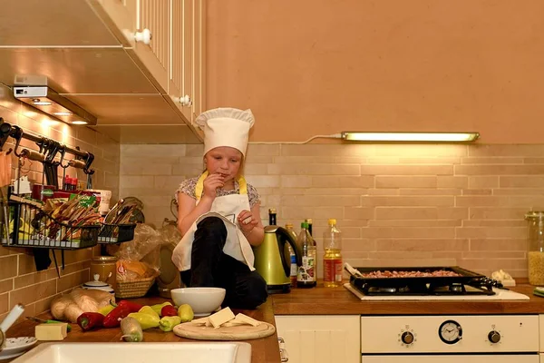 Маленькая девочка в шляпе шеф-повара на кухне. Маленькая девочка готовит пиццу . — стоковое фото