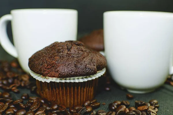 Dunkle Muffins, Tassen Kaffee und Kaffeebohnen auf schwarzem Hintergrund. — Stockfoto