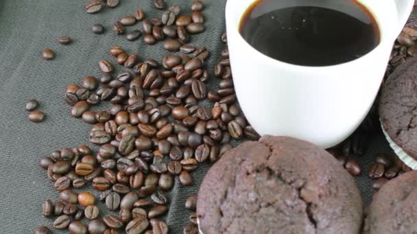 Magdalenas oscuras, taza de café y granos de café sobre fondo negro — Vídeos de Stock