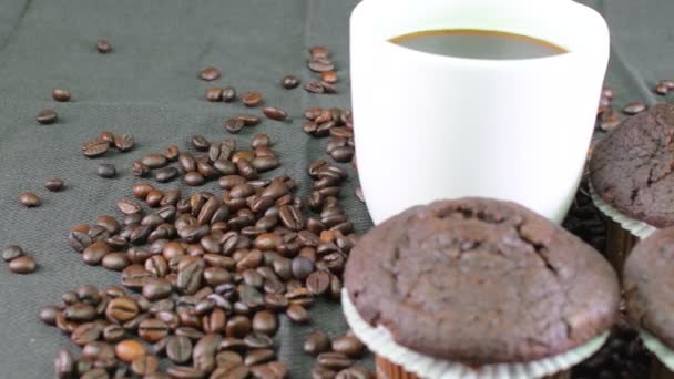 Темные кексы, чашка кофе и кофейных зерен на черном фоне — стоковое видео