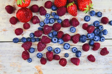 Sağlıklı karışık meyve ve çilek, ahududu, yaban mersini üst görünümden malzemelerle. Çilek beyaz rustik ahşap zemin üzerinde