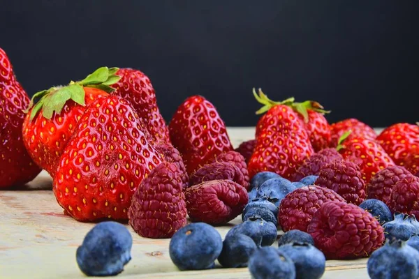 Gezonde vruchtenmengsels en ingrediënten met aardbei, framboos, bosbes. Bessen op rustieke witte houten achtergrond. Vrije ruimte voor tekst. Ruimte voor banner kopiëren — Stockfoto