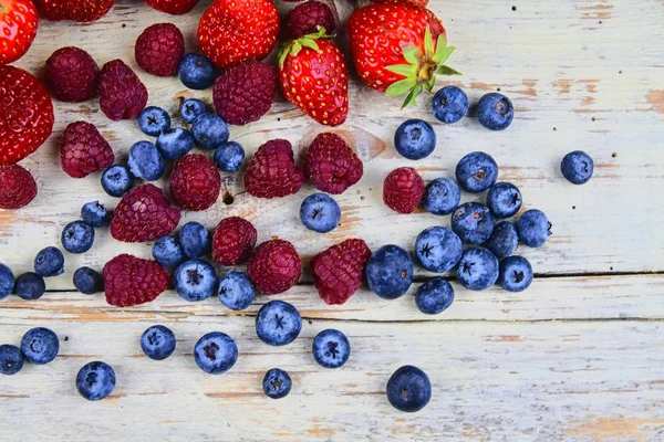 Frutta mista sana e ingredienti con fragola, lampone, mirtillo dalla vista dall'alto. Bacche su sfondo di legno bianco rustico — Foto Stock