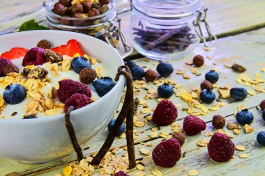 Sağlıklı kahvaltı, yoğurtlu tahıl gevreği, çilek, yabanmersini, ahududu ve müsli ahşap arka planda. Konsept: fitness, diyet, sağlık ve kahvaltı