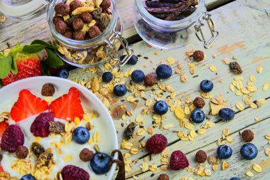 Sağlıklı kahvaltı, yoğurtlu tahıl gevreği, çilek, yabanmersini, ahududu ve müsli ahşap arka planda. Konsept: fitness, diyet, sağlık ve kahvaltı