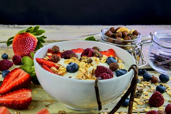 Healthy breakfast, cereal with yoghurt, strawberries, blueberries, raspberries and muesli on wooden rustic background.  Concept of: fitness, diet, wellness and breakfasts