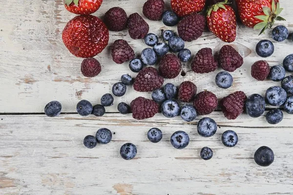 Gezonde vruchtenmengsels en ingrediënten met aardbei, framboos, bosbes van bovenaanzicht. Bessen op rustieke witte houten achtergrond — Stockfoto