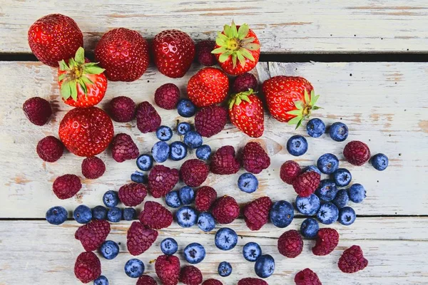 Frutta mista sana e ingredienti con fragola, lampone, mirtillo dalla vista dall'alto. Bacche su fondo rustico in legno bianco. Design piatto. Spazio libero per il testo. Copia spazio per banner — Foto Stock