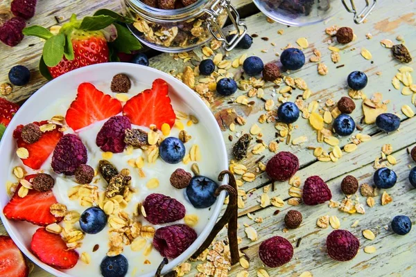 Healthy breakfast, cereal with yoghurt, strawberries, blueberries, raspberries and muesli on wooden rustic background.  Concept of: fitness, diet, wellness and breakfasts