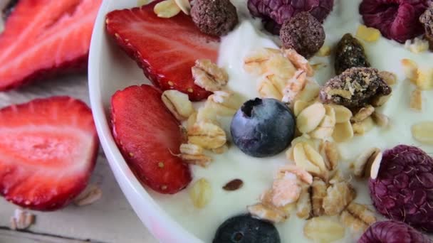 Skład z typowym śniadaniem wykonane z jogurt, borówki, maliny, jagody, musli. Pojęcia: fitness, diety, odnowy biologicznej i śniadanie. Widok z góry — Wideo stockowe