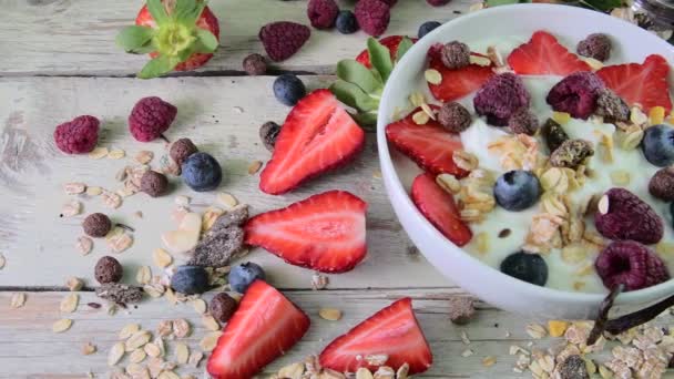 Sammansättningen av en typisk äkta frukost med yoghurt, blåbär, hallon, blåbär, müsli. Begreppet: fitness, kost, wellness och frukostar. Ovanifrån — Stockvideo