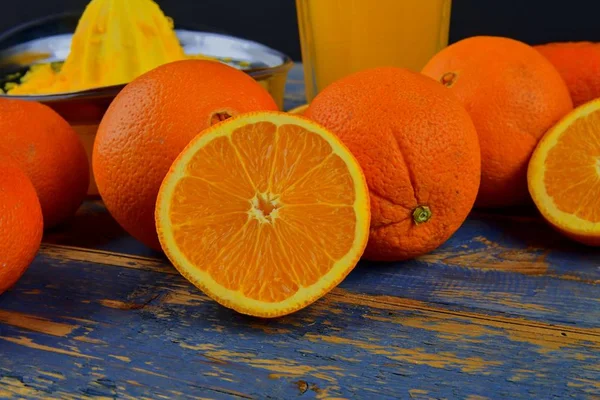 Mandarynki, pomarańcze, kieliszek soku pomarańczowego i ręczne cytrusowych squezeer na niebieskim tle drewnianych. Pomarańcze pokroić na pół — Zdjęcie stockowe