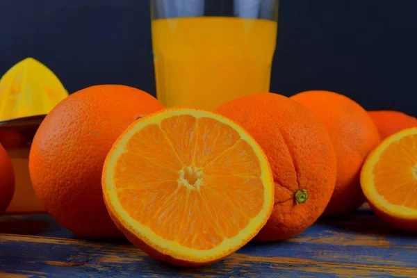 Tangerines, oranges, a glass of orange juice and manual citrus squezeer on blue wooden background. Oranges cut in half — Stock Photo, Image