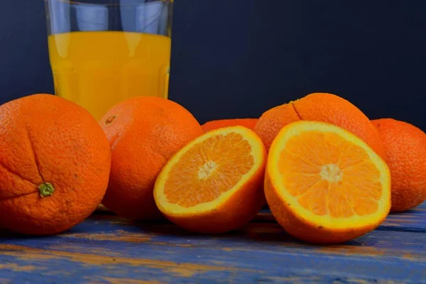 Mandarynki, pomarańcze, kieliszek soku pomarańczowego i ręczne cytrusowych squezeer na niebieskim tle drewnianych. Pomarańcze pokroić na pół. Szczelnie-do góry — Zdjęcie stockowe