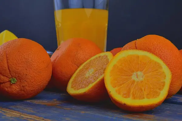 Mandarynki, pomarańcze, kieliszek soku pomarańczowego i ręczne cytrusowych squezeer na niebieskim tle drewnianych. Pomarańcze pokroić na pół — Zdjęcie stockowe