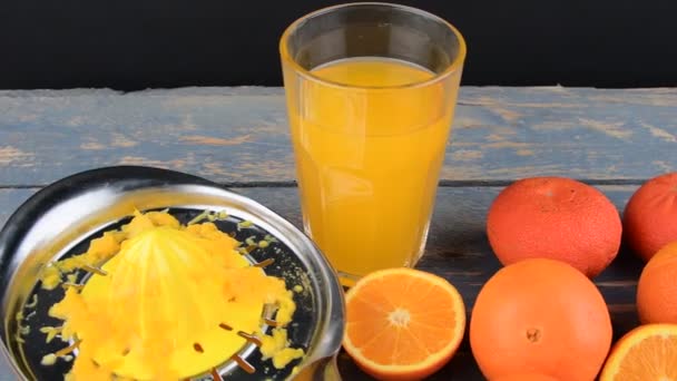 Мандарины, апельсины, стакан апельсинового сока и ручной сжиматель цитрусовых на синем деревянном фоне. Апельсины пополам — стоковое видео