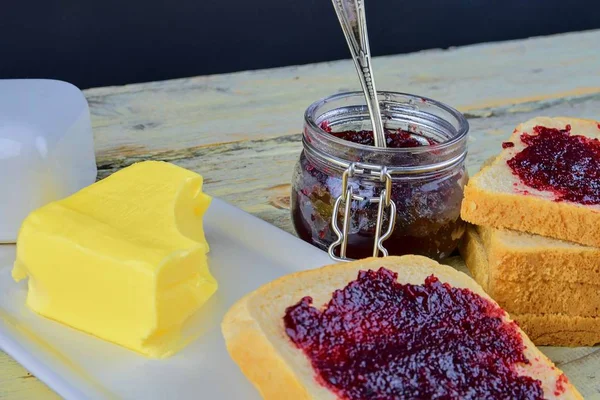 Jam, butter in butter dish and jam spread on toast.  Healthy and diet concept. Rural white wooden background.