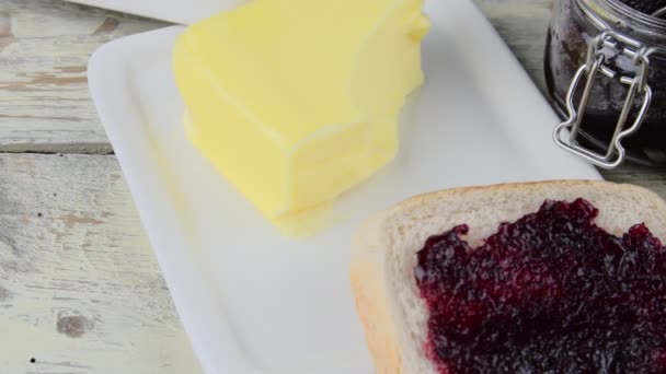 La confitura, la mantequilla en el plato de mantequilla y la mermelada se extienden sobre la tostada. Concepto saludable y dietético. Fondo rural de madera blanca — Vídeos de Stock
