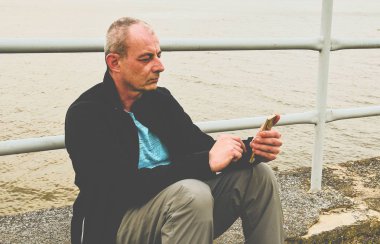 Orta göl kıyısında oturan adam yaşlı. Yalnızlık olgun adam cep telefonuyla ilgili banka. Activ adam kavramı