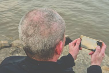 Orta göl kıyısında oturan adam yaşlı. Yalnızlık olgun adam banka selfie fotoğraf çekimi. Yalnızlık kavramını
