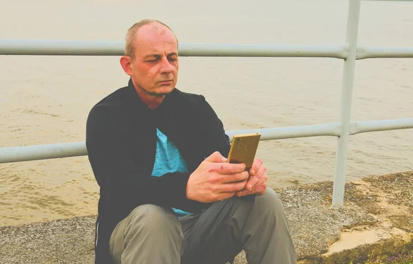 Belterület éves ember ül a tó partján. Magány érett férfi, a bank a mobiltelefon használata. Activ ember fogalmának — Stock Fotó