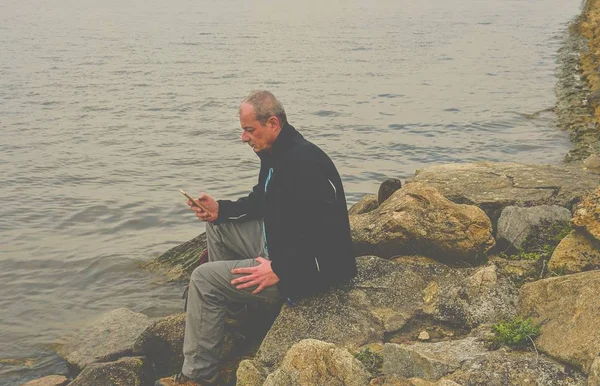 Homem de meia idade sentado na margem do lago. Solidão homem maduro usando telefone celular no banco. Conceito de homem activo — Fotografia de Stock