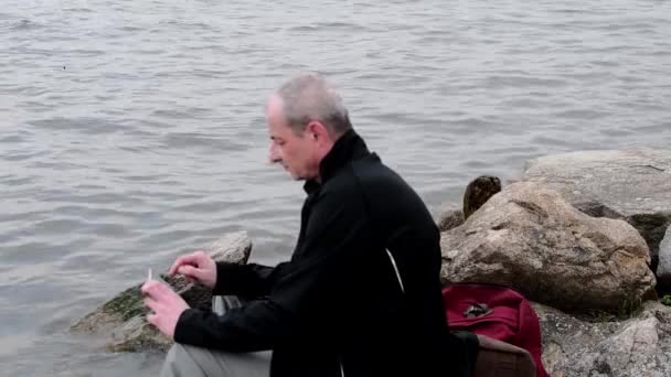 Midle äldre man som satt på stranden av sjön. Solitude mogen man med hjälp av mobiltelefon. Begreppet ensamhet — Stockvideo