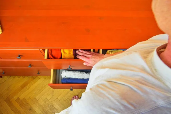 Homem organizando roupas em guarda-roupa. Homem escolhendo meias dobradas ordenadamente na gaveta. Homem a amarrar as roupas. A preparar as roupas. A ordem no peito das gavetas . — Fotografia de Stock