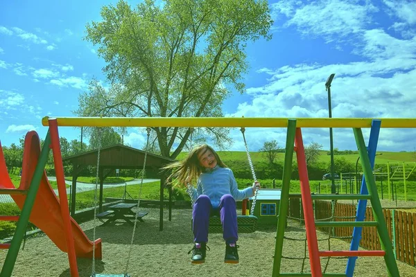 Mała dziewczynka bawiąca się na huśtawce. Mała dziewczynka latająca wysoko na huśtawce. Aktywność na świeżym powietrzu. Dzieciak bawi się. — Zdjęcie stockowe