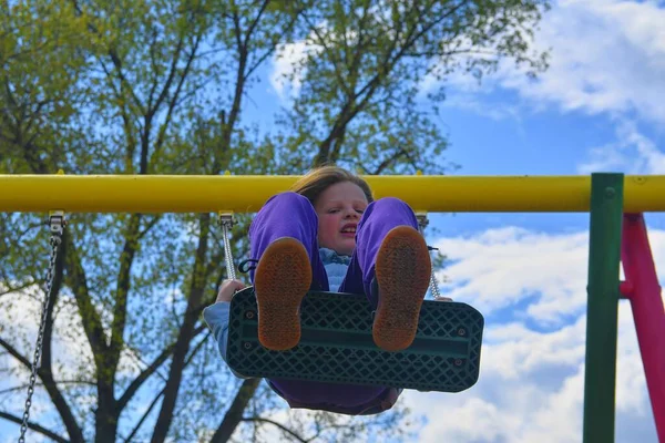 Piękna dziewczynka huśtawka na huśtawkach na placu zabaw z uśmiechem w słoneczny letni dzień. — Zdjęcie stockowe