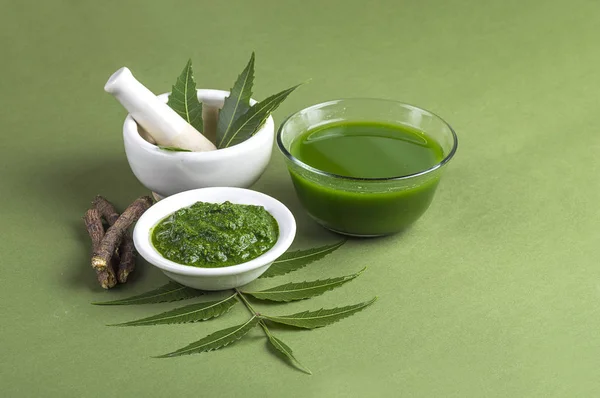 Medicinal Neem leaves in mortar and pestle with neem paste, juice and twigs on green background — Stock Photo, Image