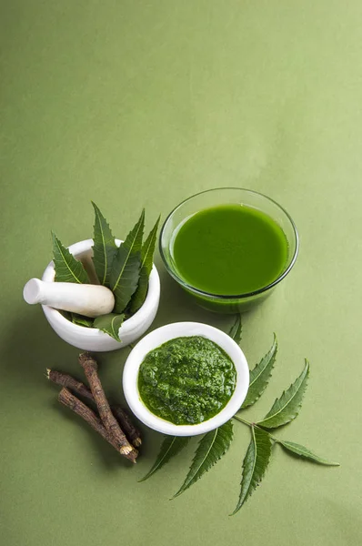 Medicinal Neem leaves in mortar and pestle with neem paste, juice and twigs on green background — Stock Photo, Image