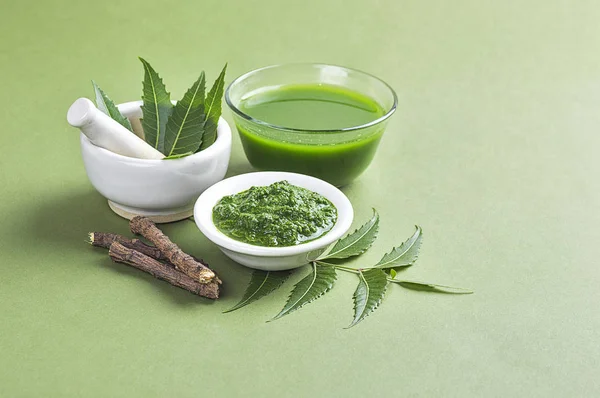 Medicinal Neem leaves in mortar and pestle with neem paste, juice and twigs on green background — Stock Photo, Image