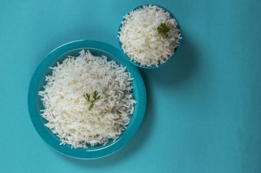 Düz beyaz basmati pirinç bir mavi plaka ve mavi arka plan üzerinde kase pişmiş