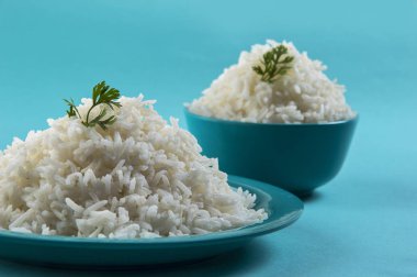 Düz beyaz basmati pirinç bir mavi plaka ve mavi arka plan üzerinde kase pişmiş