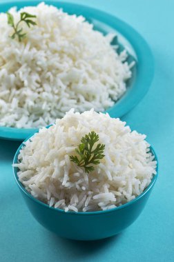 Düz beyaz basmati pirinç bir mavi plaka ve mavi arka plan üzerinde kase pişmiş