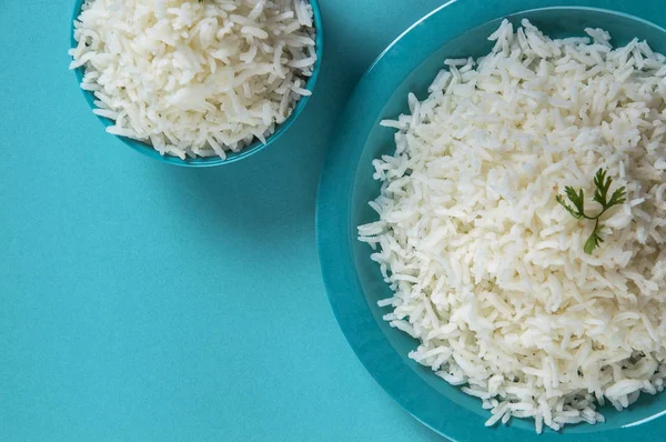 Düz beyaz basmati pirinç bir mavi plaka ve mavi arka plan üzerinde kase pişmiş