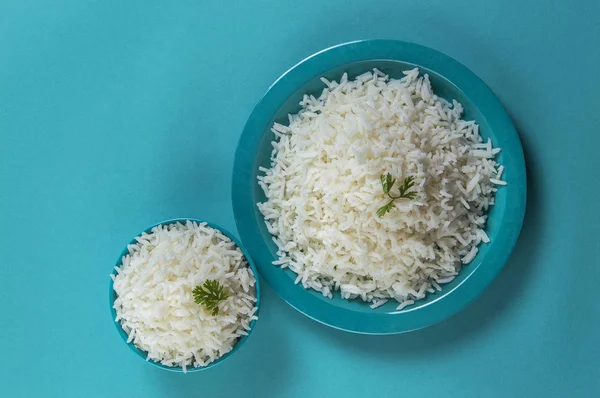 Cooked plain white basmati rice in a blue plate and bowl on blue background